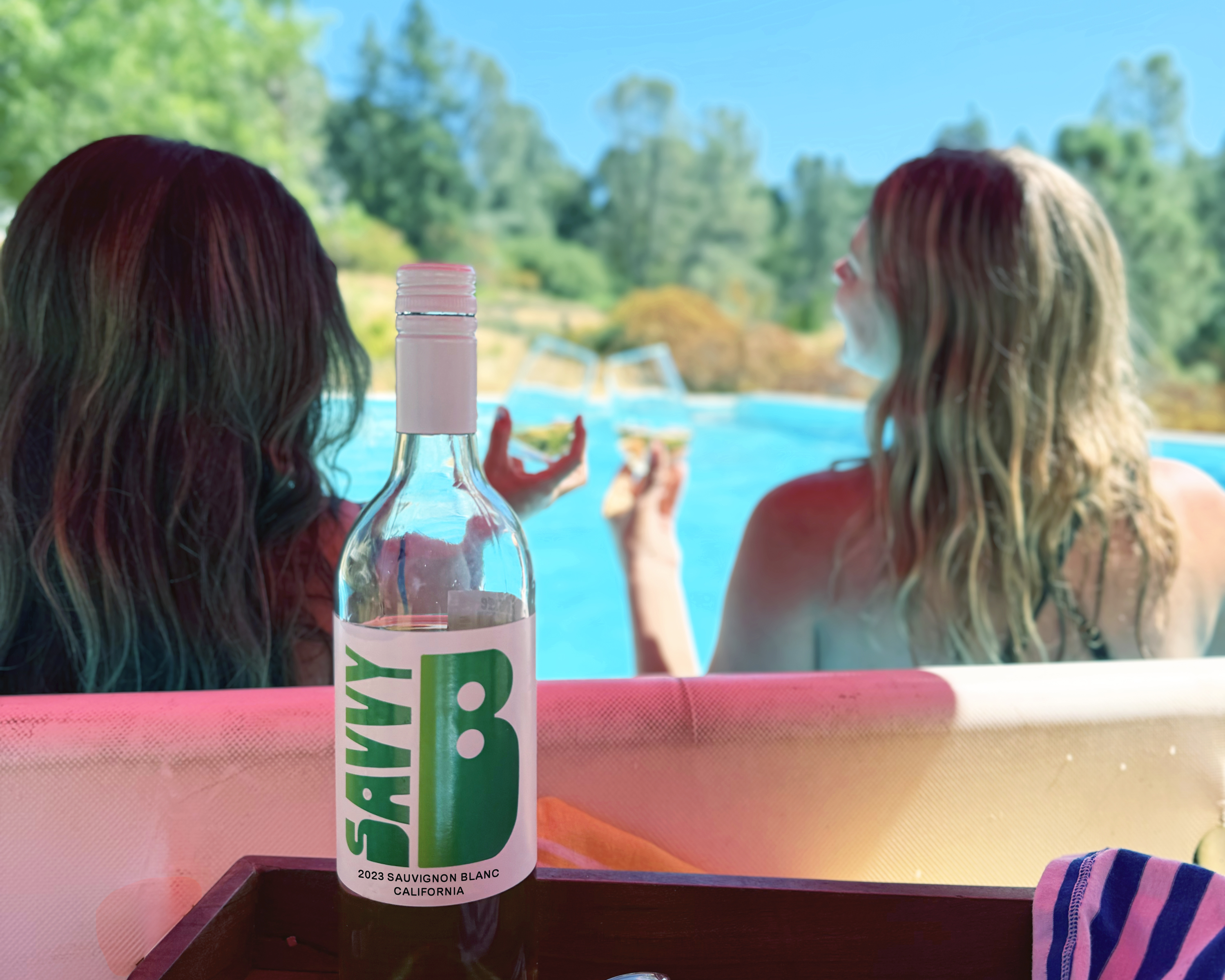 Bottle of Savvy B with people enjoying a glass poolside