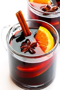 Clear glass of mulled wine with a cinnamon stick, star anise and fresh orange slice on a table.