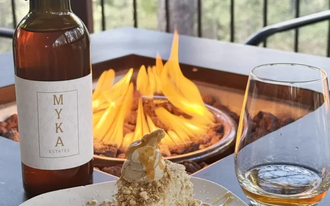 Bottle and glass of Myka wine with a slice of cheesecake by the fire